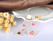 Load image into Gallery viewer, Add a playful touch to your look with these makeup elements pink lips & lipstick earrings. Crafted from rose gold color stainless steel, these charming earrings feature a fun design of pink lips and a lipstick adorned with sparkling rhinestones. Perfect for beauty lovers, they combine durability with a touch of glamour, making them a unique accessory for any outfit or a thoughtful gift for someone special.