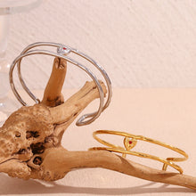 Load image into Gallery viewer, Elevate your style with this charming double layer hollow open bangle bracelet, a stunning piece that adds a touch of romance to any outfit. 18K gold plated for a luxurious finish, this bracelet features a delicate red enamel heart at the center, making it the perfect blend of elegance and playfulness. Available in both gold and silver colors, it's a versatile accessory that can easily complement any look, from casual to chic.