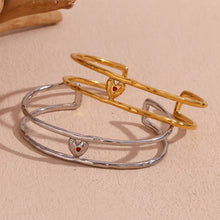 Load image into Gallery viewer, Elevate your style with this charming double layer hollow open bangle bracelet, a stunning piece that adds a touch of romance to any outfit. 18K gold plated for a luxurious finish, this bracelet features a delicate red enamel heart at the center, making it the perfect blend of elegance and playfulness. Available in both gold and silver colors, it's a versatile accessory that can easily complement any look, from casual to chic.