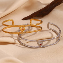 Load image into Gallery viewer, Elevate your style with this charming double layer hollow open bangle bracelet, a stunning piece that adds a touch of romance to any outfit. 18K gold plated for a luxurious finish, this bracelet features a delicate red enamel heart at the center, making it the perfect blend of elegance and playfulness. Available in both gold and silver colors, it's a versatile accessory that can easily complement any look, from casual to chic.