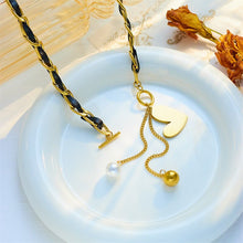 Load image into Gallery viewer, This statement rock glam necklace is made of stainless steel and leather strap. It has nice toggle clasp with a black heart hanging on it. There are two chains hanging from the heart that are endings with a gold and a white pearl. It is a perfect piece for an elegant occasion outfit as well as a nice gift for your special ones.