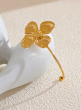 Load image into Gallery viewer, Embrace bold elegance with this stunning charm metal flower cuff bracelet, a statement piece designed to captivate. Featuring an intricate large flower motif, this open bangle is crafted from high-quality stainless steel and plated in radiant 18K gold for a luxurious finish. Its sleek, thin band beautifully contrasts with the striking floral design, creating a unique balance of sophistication and flair.