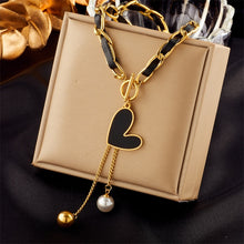 Load image into Gallery viewer, This statement rock glam necklace is made of stainless steel and leather strap. It has nice toggle clasp with a black heart hanging on it. There are two chains hanging from the heart that are endings with a gold and a white pearl. It is a perfect piece for an elegant occasion outfit as well as a nice gift for your special ones.