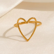 Load image into Gallery viewer, Fall in love with the effortless charm of this stainless steel hollow heart ring — a minimalistic statement piece with a romantic twist. Featuring a sleek open design and a delicate heart-shaped cutout, this ring blends Western-inspired style with modern simplicity. Available in both polished silver and radiant gold finishes, it's the perfect accessory for adding a subtle touch of elegance to your everyday look or party outfit. Durable, waterproof, and endlessly versatile, it also makes a thoughtful gift th