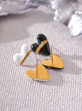 Load image into Gallery viewer, These trendy heart stud earrings feature a chic black or white enamel finish, adorned with a delicate golden chain that adds a unique touch of elegance. Crafted from high-quality 18K plated stainless steel, they exude lasting charm and sophistication. Their romantic design combines classic style with a modern twist, making them a perfect accessory for women who love eye-catching yet versatile jewelry.