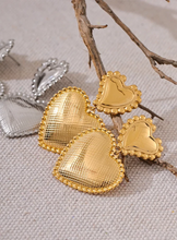Load image into Gallery viewer, These romantic drop earrings feature an enchanting design with a larger heart gracefully dangling from a smaller one, each crafted from hypoallergenic stainless steel and plated in radiant 18K gold or classic silver. The textured surface and intricate edges add depth and charm, creating an eye-catching look that's both elegant and playful.