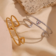 Load image into Gallery viewer, Elevate your style with this charming double layer hollow open bangle bracelet, a stunning piece that adds a touch of romance to any outfit. 18K gold plated for a luxurious finish, this bracelet features a delicate red enamel heart at the center, making it the perfect blend of elegance and playfulness. Available in both gold and silver colors, it's a versatile accessory that can easily complement any look, from casual to chic.