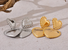Load image into Gallery viewer, These romantic drop earrings feature an enchanting design with a larger heart gracefully dangling from a smaller one, each crafted from hypoallergenic stainless steel and plated in radiant 18K gold or classic silver. The textured surface and intricate edges add depth and charm, creating an eye-catching look that's both elegant and playful.