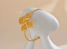 Load image into Gallery viewer, Embrace bold elegance with this stunning charm metal flower cuff bracelet, a statement piece designed to captivate. Featuring an intricate large flower motif, this open bangle is crafted from high-quality stainless steel and plated in radiant 18K gold for a luxurious finish. Its sleek, thin band beautifully contrasts with the striking floral design, creating a unique balance of sophistication and flair.