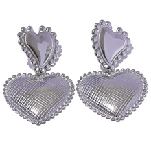 Load image into Gallery viewer, These romantic drop earrings feature an enchanting design with a larger heart gracefully dangling from a smaller one, each crafted from hypoallergenic stainless steel and plated in radiant 18K gold or classic silver. The textured surface and intricate edges add depth and charm, creating an eye-catching look that's both elegant and playful.