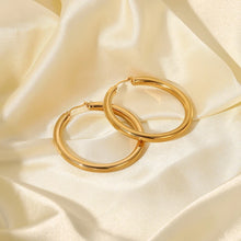 Load image into Gallery viewer, Make a bold statement with these chunky geometric gold plated hollow hoop earrings. Featuring a sleek, thick design and crafted from durable stainless steel, these big circle hoops offer a modern yet timeless look. Their radiant gold plating adds a touch of luxury, making them perfect for both everyday wear and special occasions. A chic and versatile accessory for any jewelry collection!