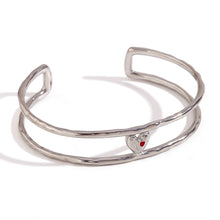 Load image into Gallery viewer, Elevate your style with this charming double layer hollow open bangle bracelet, a stunning piece that adds a touch of romance to any outfit. 18K gold plated for a luxurious finish, this bracelet features a delicate red enamel heart at the center, making it the perfect blend of elegance and playfulness. Available in both gold and silver colors, it's a versatile accessory that can easily complement any look, from casual to chic.