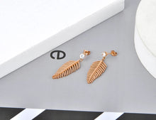 Load image into Gallery viewer, Elegant stainless steel earrings are made in a rose gold colour. They consists of small cubic zirconia on which a leave of fern is hanging. The surface of the fern is sanded which gives the earrings special look. Earrings are rose gold plated and represent great accessory to your elegant outfit. They have stud fastening.
