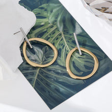 Load image into Gallery viewer, Fashionable and trendy metal earrings are made in a combination of gold and silver colour. They consists of a gold and irregular hollow circle which hangs on a silver stick. Their simplicity gives them very special and glamorous look. Earrings has real gold plating and represent perfect and elegant touch to any outfit. They have stud fastening.
