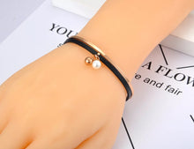 Load image into Gallery viewer, Bangle bracelet is made of stainless steel and comes in rose gold variant. It is adorned with black leather strip and two small balls. One of the balls is in rose gold colour and the other is pearl white. It is perfect accessory for going out.