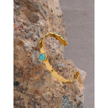 Load image into Gallery viewer, Bangle bracelet is made of stainless steel and it has real gold plating. It comes in gold colour and it is adorned with a beautiful blue stone. Its borders have carvings and interesting structure. It is a perfect accessory for winter or summer outfit.