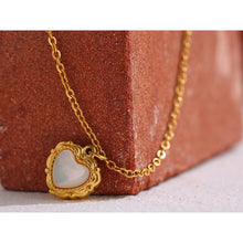 Load image into Gallery viewer, Necklace is made of stainless steel and comes in a gold colour with real gold plating. It is made of a thin elegant chain that is adorned with a heart pedant. Heart pedant is made of shell and it is circled with stainless steel border with interesting engravings. Necklace is a very elegant piece that will glam up your outfit. It has adjustable length and lobster clasp.