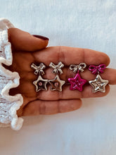 Load image into Gallery viewer, Hand holding small star-shaped earrings with a plain background
