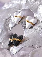 Load image into Gallery viewer, These trendy heart stud earrings feature a chic black or white enamel finish, adorned with a delicate golden chain that adds a unique touch of elegance. Crafted from high-quality 18K plated stainless steel, they exude lasting charm and sophistication. Their romantic design combines classic style with a modern twist, making them a perfect accessory for women who love eye-catching yet versatile jewelry.
