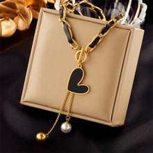 Load image into Gallery viewer, This statement rock glam necklace is made of stainless steel and leather strap. It has nice toggle clasp with a black heart hanging on it. There are two chains hanging from the heart that are endings with a gold and a white pearl. It is a perfect piece for an elegant occasion outfit as well as a nice gift for your special ones.
