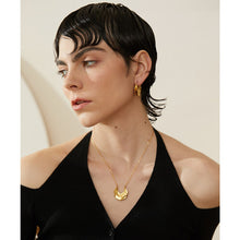 Load image into Gallery viewer, Statement stainless steel necklace comes in a gold colour. It is made of fine thin chain and it is adorned with a nice pendant in the shape of the crescent moon. Interesting shape of the pendant and its irregular surface makes this necklace very glamorous and interesting to be added to any outfit.. It has lobster clasp and adjustable length.
