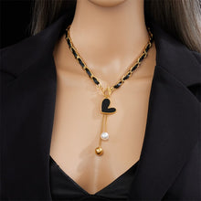 Load image into Gallery viewer, This statement rock glam necklace is made of stainless steel and leather strap. It has nice toggle clasp with a black heart hanging on it. There are two chains hanging from the heart that are endings with a gold and a white pearl. It is a perfect piece for an elegant occasion outfit as well as a nice gift for your special ones.
