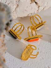 Load image into Gallery viewer, Make a statement with this striking square geometric open ring, featuring a bold, big stone available in four captivating colors: black, red, white, and green. Each stone is beautifully framed by a notched gold edge, adding texture and a luxurious touch to this modern design. Crafted from durable stainless steel and finished with high-quality gold plating, this wide, adjustable ring combines elegance with a contemporary twist, offering a perfect fit and lasting shine.
