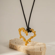 Load image into Gallery viewer, This glam rock necklace is made of gold plated stainless steel pendant which is hanging on a black wax rope. The hollow heart pendant comes in two colours: gold and silver. Its shape imitates lava, which gives the necklace an interesting look. It is a perfect piece for any daily occasion. 
