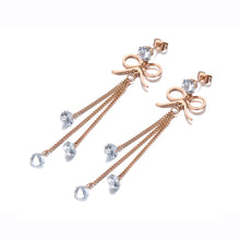 Load image into Gallery viewer, These beautiful bohemian earrings are made of stainless steel which is three times gold plated.  They come in a rose gold colour. They have one bigger cubic zirconia under which cute little bowknot is situated. Three delicate chains are hanging from the bowknot and each ends with a small transparent cubic zirconia. Earrings makes perfect accessory for your evening outfit. They have stud closure.
