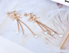 Load image into Gallery viewer, These beautiful bohemian earrings are made of stainless steel which is three times gold plated.  They come in a rose gold colour. They have one bigger cubic zirconia under which cute little bowknot is situated. Three delicate chains are hanging from the bowknot and each ends with a small transparent cubic zirconia. Earrings makes perfect accessory for your evening outfit. They have stud closure.
