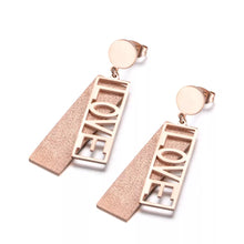 Load image into Gallery viewer, These fashionable stainless steel earrings are made in a rose gold colour or combination of silver and rose gold. They consists of a sanded rectangle and letters LOVE. Both, letters and rectangle are hanging on a circle.Earrings are three times gold plated and represent perfect and elegant touch to your day to day style. They have stud fastening.
