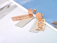 Load image into Gallery viewer, These fashionable stainless steel earrings are made in a rose gold colour or combination of silver and rose gold. They consists of a sanded rectangle and letters LOVE. Both, letters and rectangle are hanging on a circle.Earrings are three times gold plated and represent perfect and elegant touch to your day to day style. They have stud fastening.
