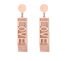 Load image into Gallery viewer, These fashionable stainless steel earrings are made in a rose gold colour or combination of silver and rose gold. They consists of a sanded rectangle and letters LOVE. Both, letters and rectangle are hanging on a circle.Earrings are three times gold plated and represent perfect and elegant touch to your day to day style. They have stud fastening.
