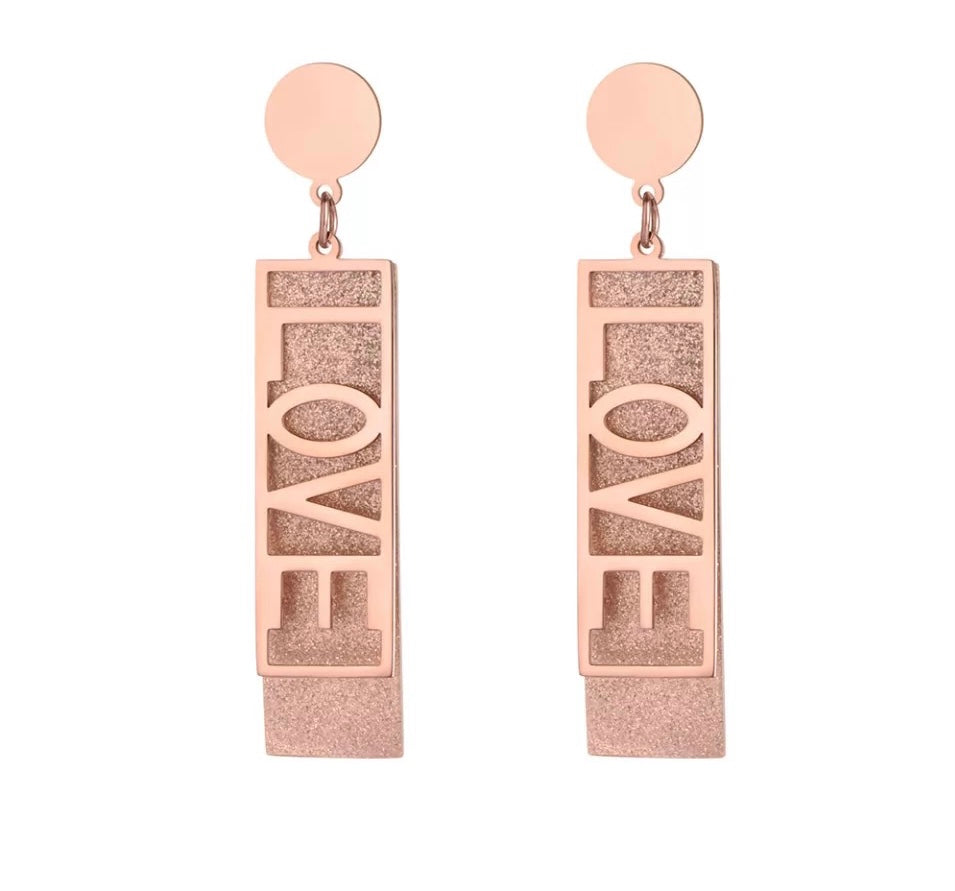 These fashionable stainless steel earrings are made in a rose gold colour or combination of silver and rose gold. They consists of a sanded rectangle and letters LOVE. Both, letters and rectangle are hanging on a circle.Earrings are three times gold plated and represent perfect and elegant touch to your day to day style. They have stud fastening.