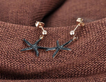 Load image into Gallery viewer, Trendy stainless steel earrings are made in a rose gold colour. They are adorned with starfish that comes in white or black colour. Starfish is made of cubic zirconia and it hangs on a little ball. Earrings are rose gold plated and made great summer accessory. They have stud fastening.
