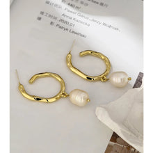 Load image into Gallery viewer, Elegant metal earrings are made in a gold colour. They consists of a big irregular hoop on which a natural pearl is attached. Earrings has real gold plating and represent perfect and elegant touch to your classy and elegant outfit. They have stud fastening.
