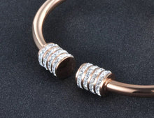 Load image into Gallery viewer, Elegant and luxurious bangle bracelet is made of stainless steel. It comes in two colours: rose gold and silver. It is adorned with rollers on each of its ends. Rollers have lines of embedded cubic zirconia in silver colour. It is a perfect bracelet for glamorous evening. 
