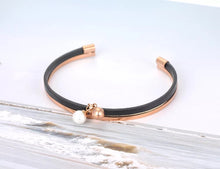 Load image into Gallery viewer, Bangle bracelet is made of stainless steel and comes in rose gold variant. It is adorned with black leather strip and two small balls. One of the balls is in rose gold colour and the other is pearl white. It is perfect accessory for going out. 
