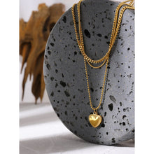 Load image into Gallery viewer, Stainless steel necklace comes in a gold colour and it is three times gold plated. This layered necklace is made of three different chains. The longest one is adorned with a little pedant in a shape of a heart. The heart is decorated with small engraved circles around its border. The chain necklace is perfect for any outfit. It has adjustable length and lobster clasp.
